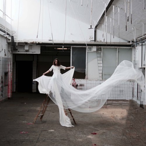 In einer verlassenen Fleischerhalle steht ein Model in einem weissen Kleid auf einer Leiter.