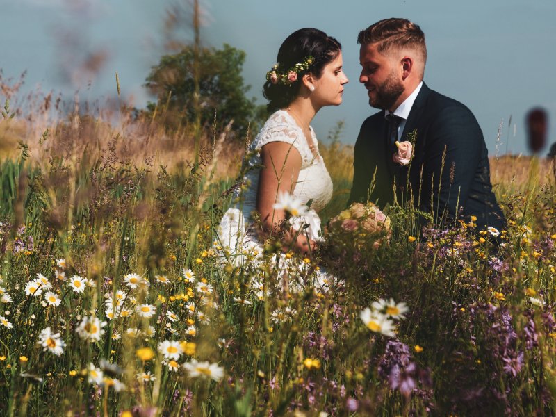 Hochzeitsfoto von dem Ehepaar Madeline und Michael, waehrend sie in einer Blumenwiese sitzen.