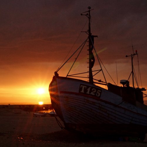 Ein gestrandetes Boot mit dem Namen T125 wurde im Sonnenuntergang fotografiert.